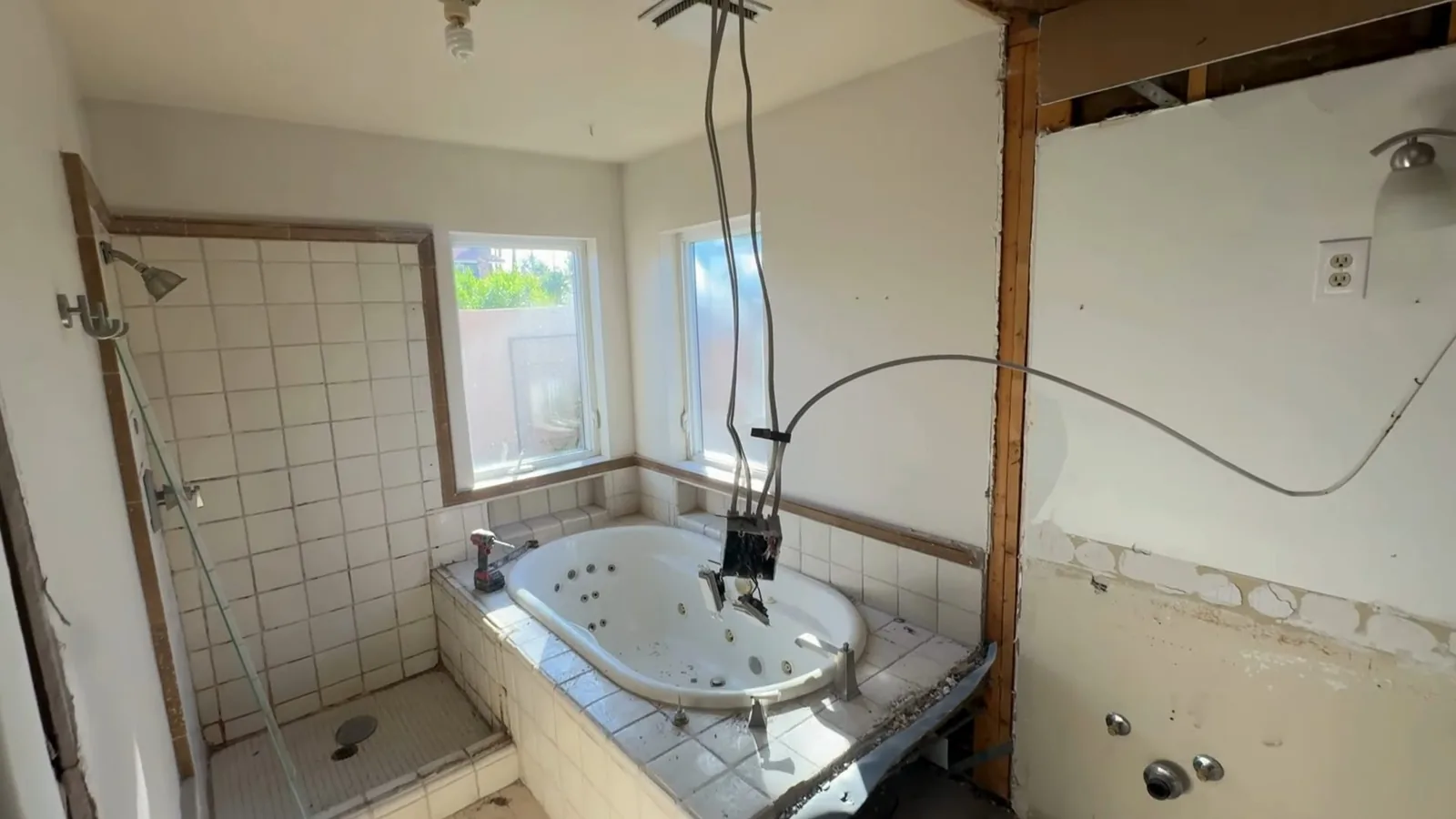 Bathroom with wall sections removed to the studs around a jetted tub, tile on part of the wall and cords hanging from the ceiling