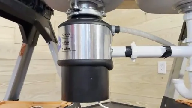 Garbage disposal mounted on a frame with a white discharge pipe, a ribbed hose and a drain trap beside it