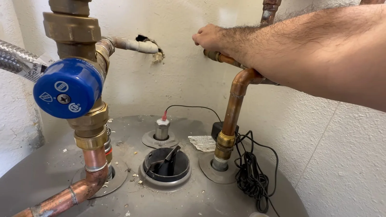 Hand resting on copper supply pipes where they connect to the top of a tank water heater, with a blue-capped valve at left