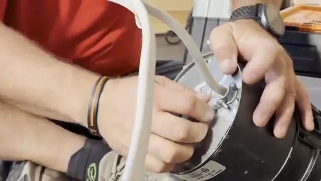Hands fastening a white electrical cable to the base plate of a disposal motor