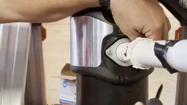 Hands working at the mounting ring and discharge connection of a stainless disposal, with a black-taped white pipe coming off the side