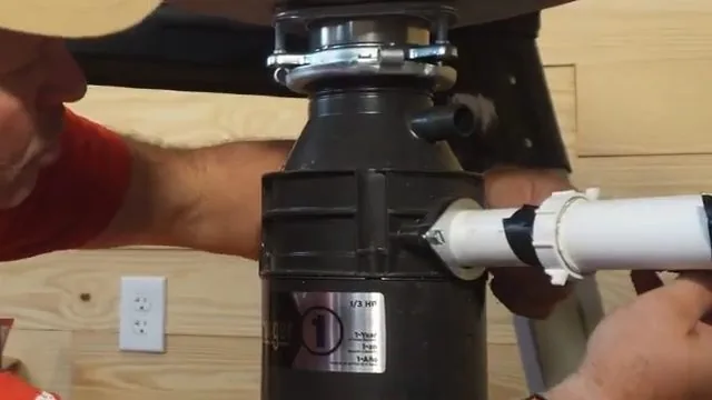 Man in a red shirt and cap connecting a white discharge pipe to the side of a black garbage disposal
