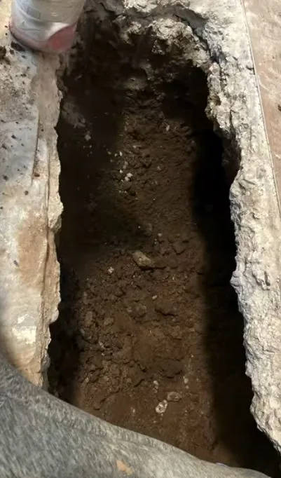 Narrow opening in a broken concrete floor with dark soil visible beneath it