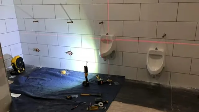 Tiled restroom wall with two urinals, red laser lines and tools laid out on a dark tarp
