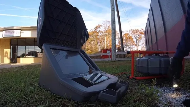 Open sewer camera control unit sitting on grass in front of a low commercial building, with a cable reel at the right