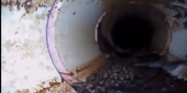 Camera view down a pipe showing a joint ring and debris collected at the bottom