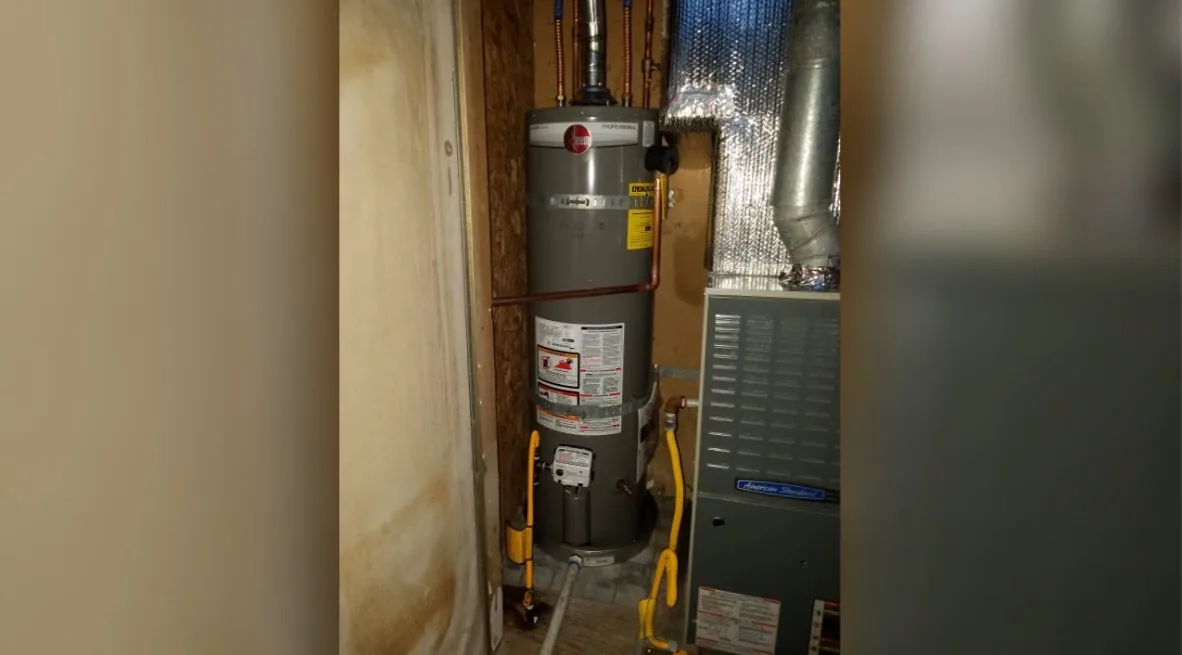 Tank water heater and a furnace side by side in a narrow closet, with a vent pipe above and a yellow gas line at the bottom