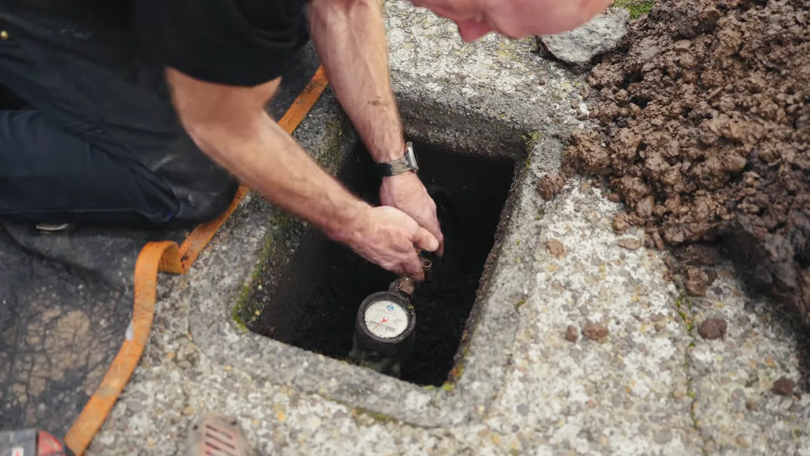 Technician kneeling beside an open concrete meter box with a water meter at the bottom
