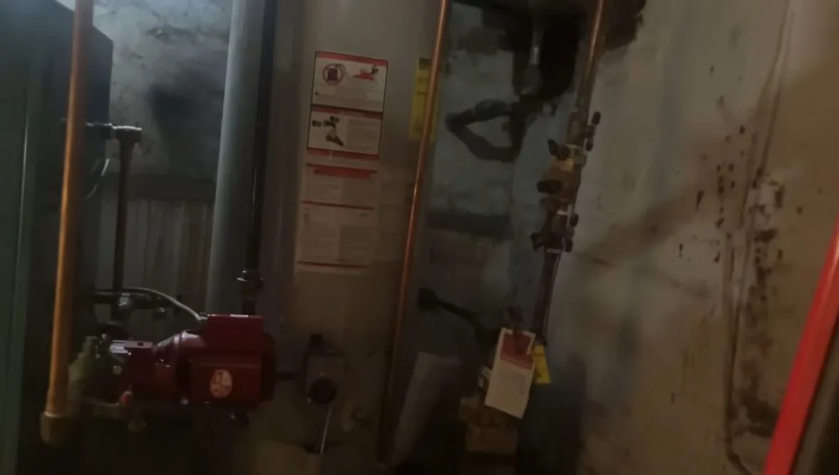 Utility room wall with copper and steel pipes, valves and red equipment, with warning labels on the wall