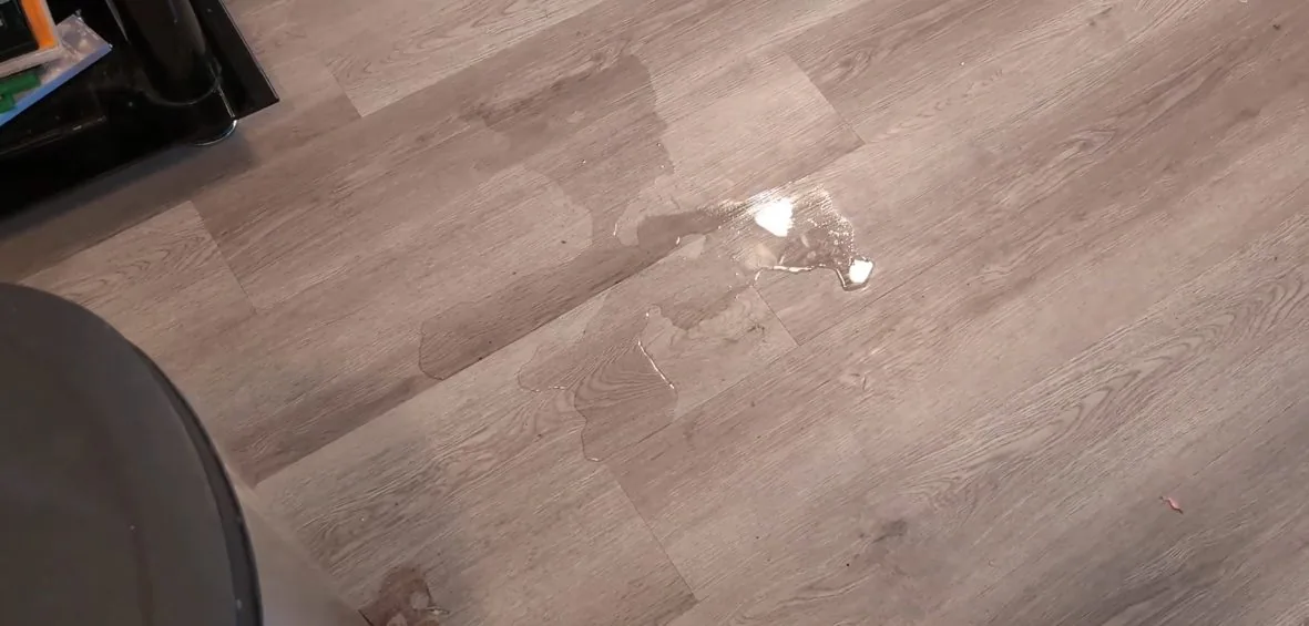 Small puddle and wet patches on a gray wood-look plank floor