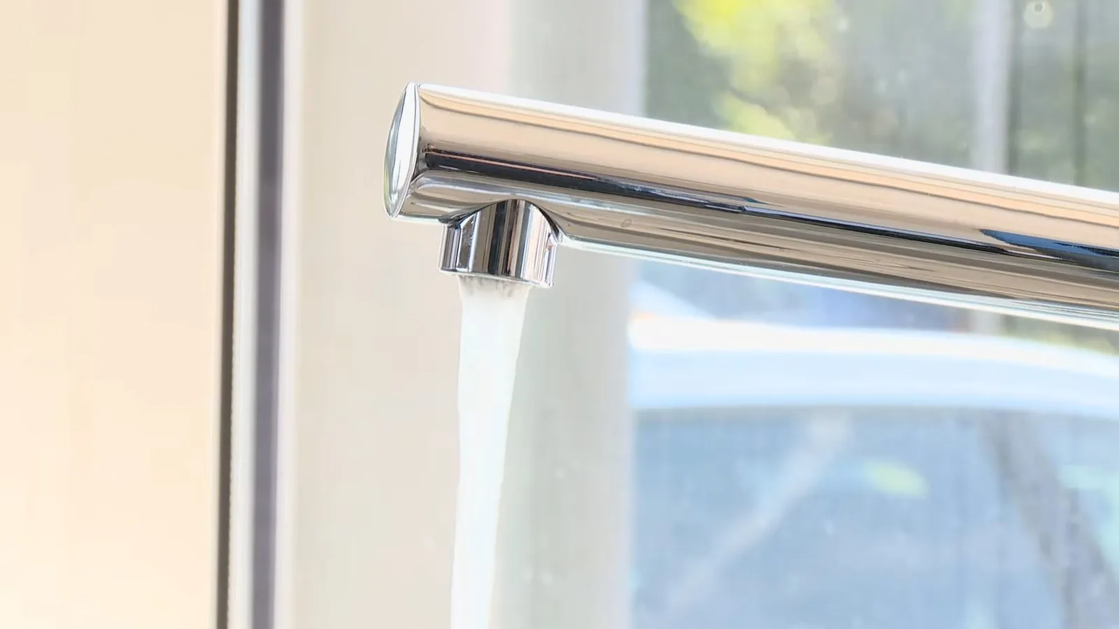 Chrome kitchen faucet with water running from the spout, beside a bright window