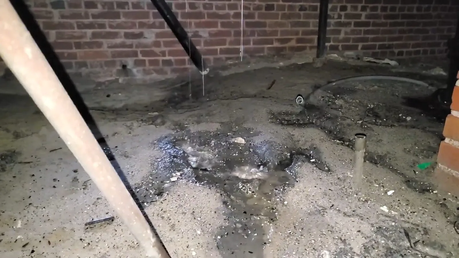 Crawl space with wet, dark ground, a brick foundation wall and water dripping from a pipe above