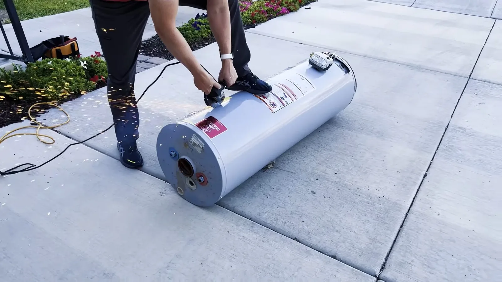 Person standing over a white tank water heater lying on a hand truck on a concrete sidewalk